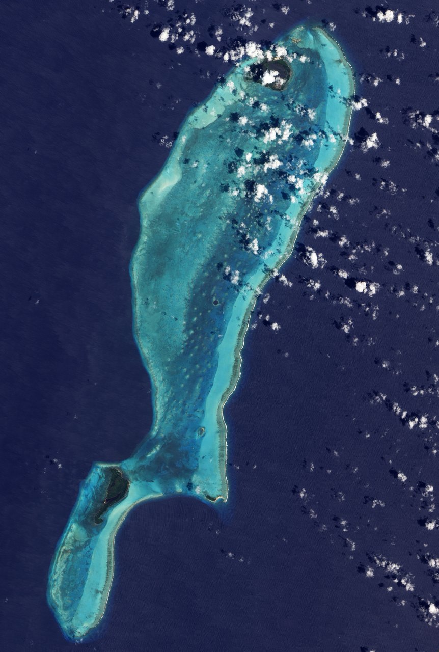 EO-1 satellite view of turquoise Lighthouse Reef off Belize, with a small dark circular Blue Hole amid shallow water and scattered clouds.