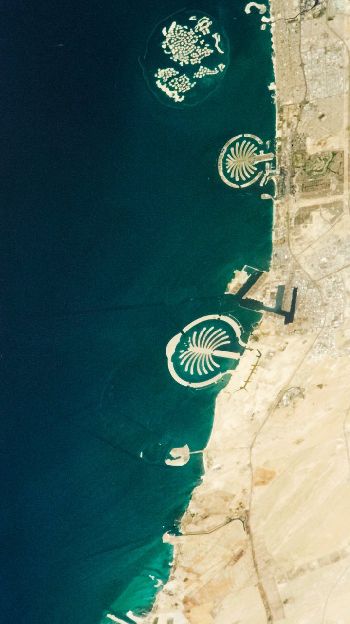 Astronaut view of Dubai’s coast, with palm-shaped artificial islands and The World archipelago against dark Gulf waters.